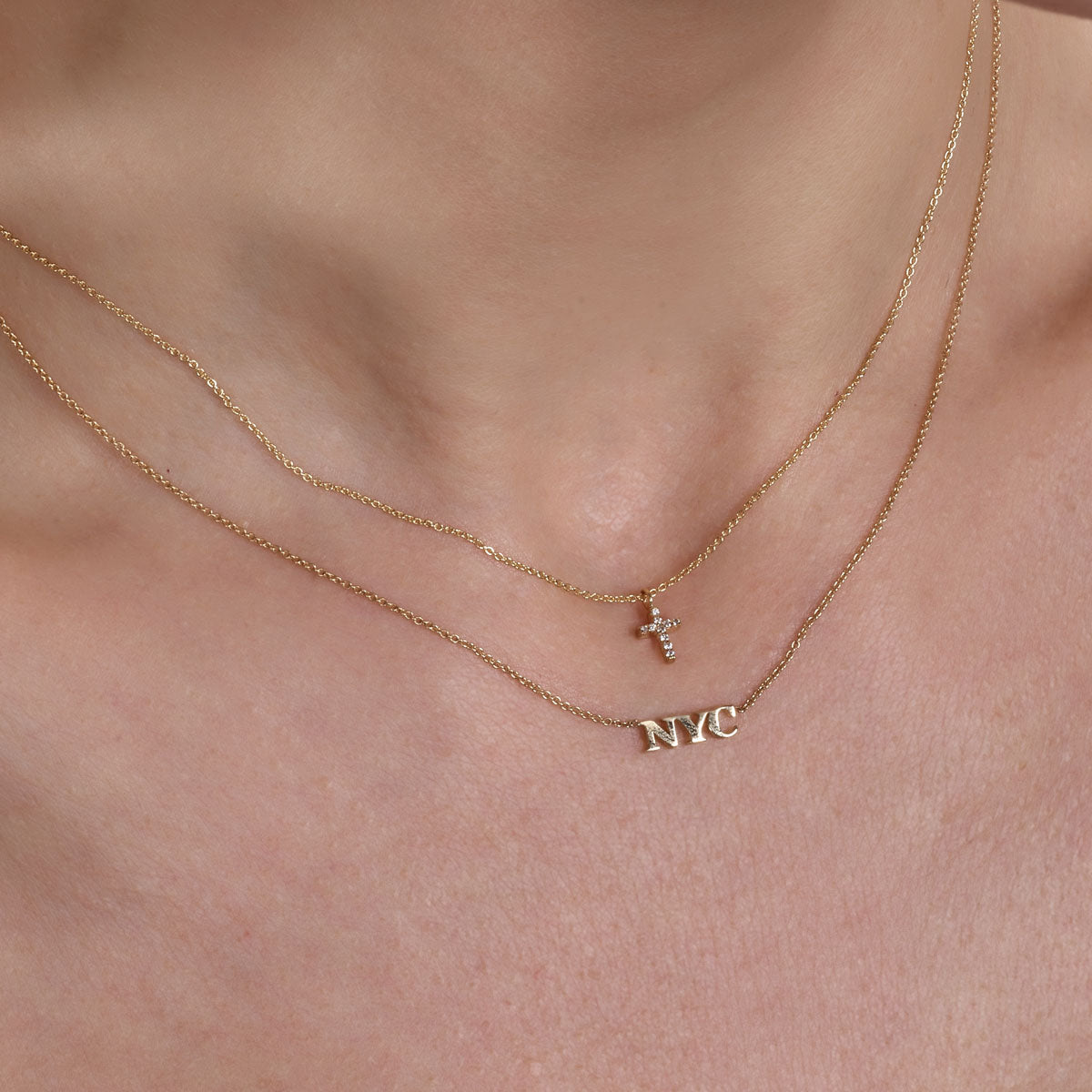 Gold diamond cross and NYC necklaces on neck - layered faith and city-inspired jewelry