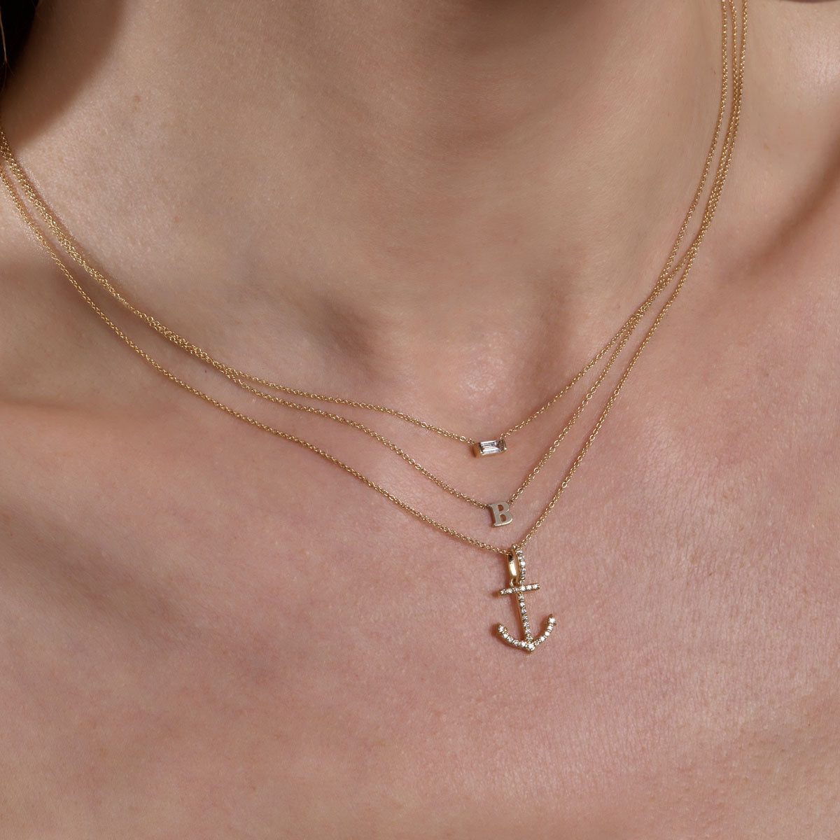 Gold diamond rectangle, initial, and anchor necklaces on neck.