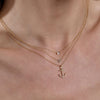 Gold diamond rectangle, initial, and anchor necklaces on neck.